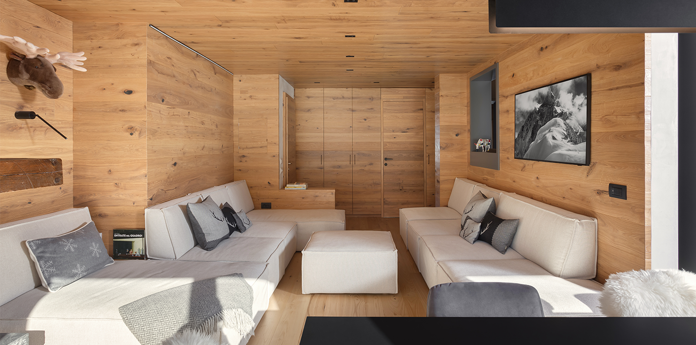 Interno di un appartamento di montagna. Soffitti, pareti e arredo su misura rivestiti in listoni di legno di quercia piallati a mano. Parquet in castagno. Divani modulari realizzati su misura.