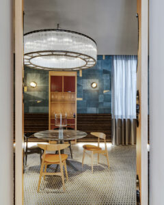 Sala da pranzo dal design elegante e contemporaneo, con tavolo rotondo in marmo, sedie in legno e grande lampadario circolare sospeso. Le pareti combinano pannelli geometrici blu e dettagli caldi in legno, creando un ambiente raffinato e accogliente.