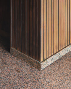 Parte di un muro in legno a listelli con un angolo e una base in granito, su un pavimento in granito.