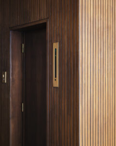 Una parete in legno a doghe verticali con una porta e un segnalatore di piano dell'ascensore.