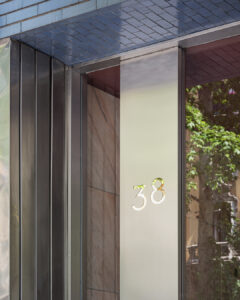 Numero civico inciso su piastra verticale in acciaio satinato della parete vetrata d'ingresso all'androne del palazzo